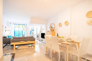 Un salon moderne avec un canapé, une table à manger dressée pour quatre personnes et un téléviseur.