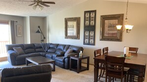 A living room with a sectional sofa, a coffee table, a dining table with chairs, and a chandelier. - Hunting, Fishing and River-fun Getaway! (Pierre)