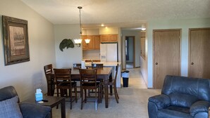 A living room with a dark leather sofa, a dining area with wooden chairs and a table, and a kitchen with wooden cabinets and a refrigerator. - Hunting, Fishing and River-fun Getaway! (Pierre)