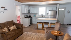 Une cuisine moderne avec des meubles blancs, un four à micro-ondes, une cuisinière et un réfrigérateur. On y trouve également un coin repas avec un canapé marron et une petite table ronde.