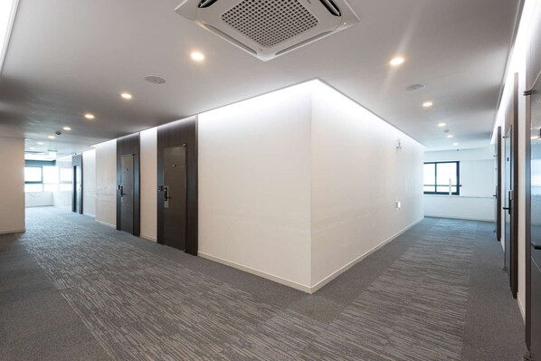 Un espacio de oficina moderno con un diseño limpio y minimalista, que presenta una pared blanca grande, puertas de madera oscura y piso alfombrado.