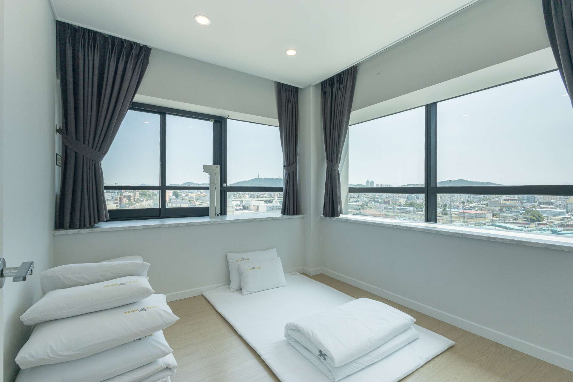 A hotel room with large windows, a bed with white bedding, and a view of the cityscape.