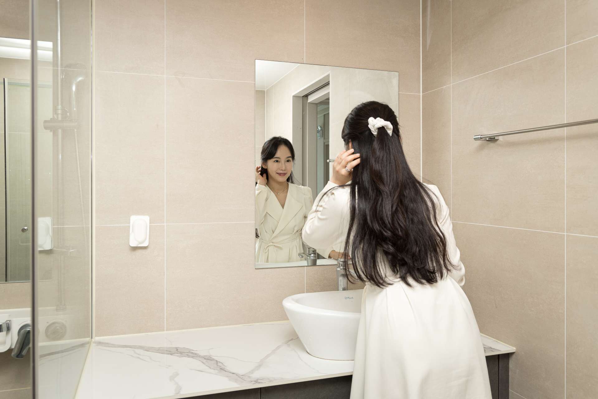 A modern bathroom with a large mirror, a white sink, and a glass shower enclosure.