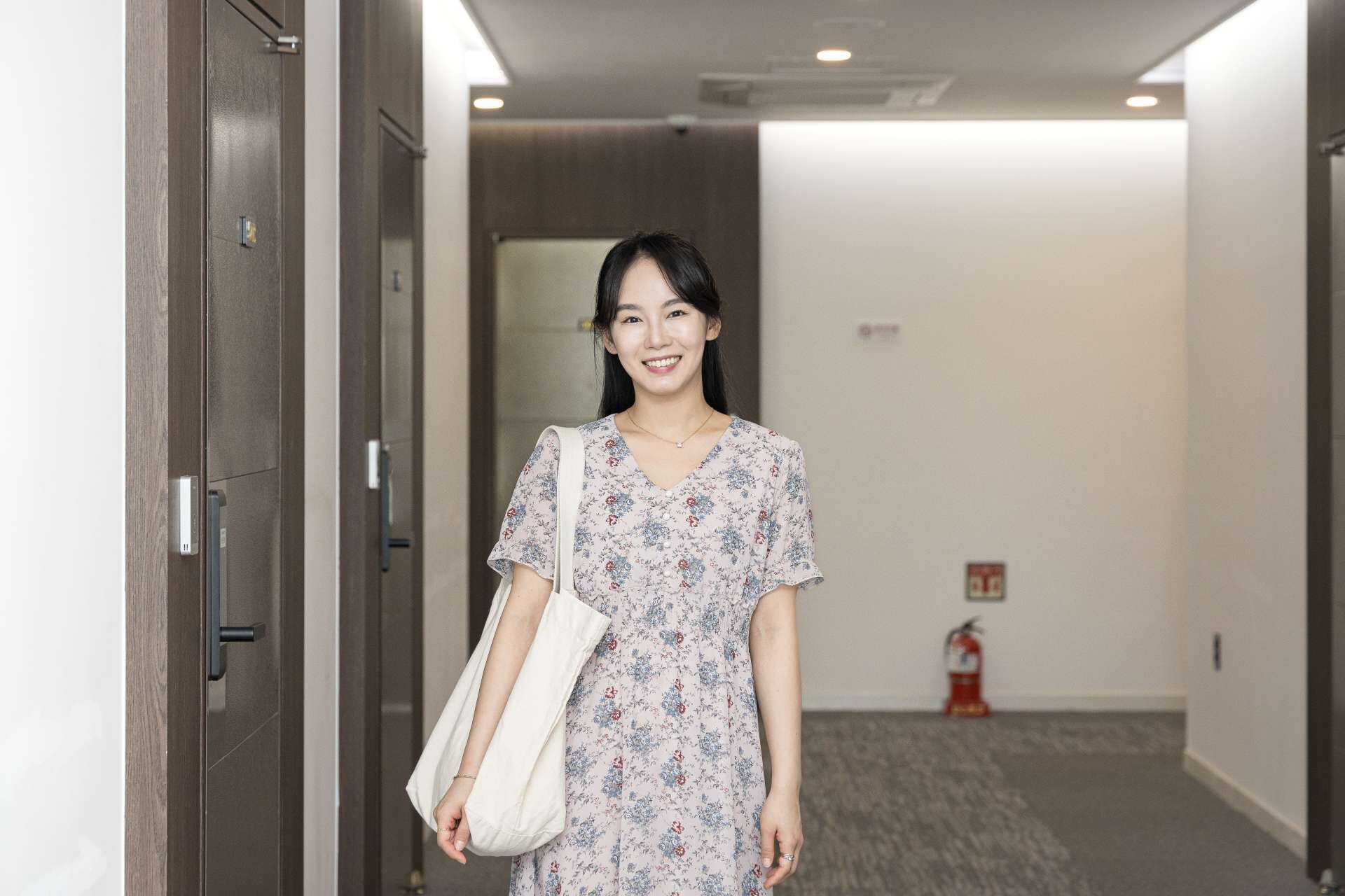 Uma mulher de vestido floral está em um corredor com um extintor na parede.