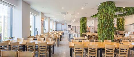 A spacious dining area with multiple tables and chairs, a central serving counter, and a large vertical garden feature.