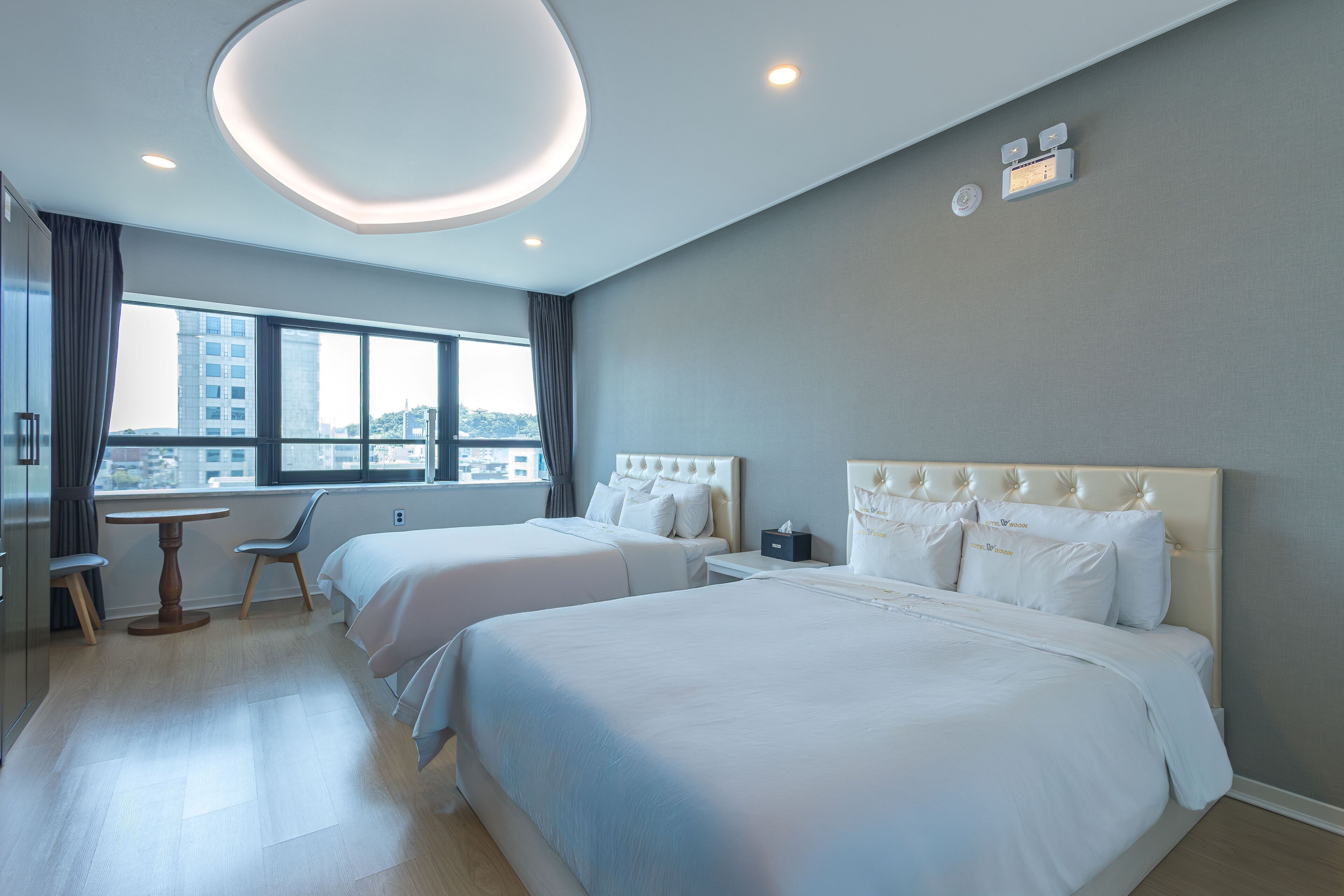 A hotel room with two beds, a dining table, and a view of the city.