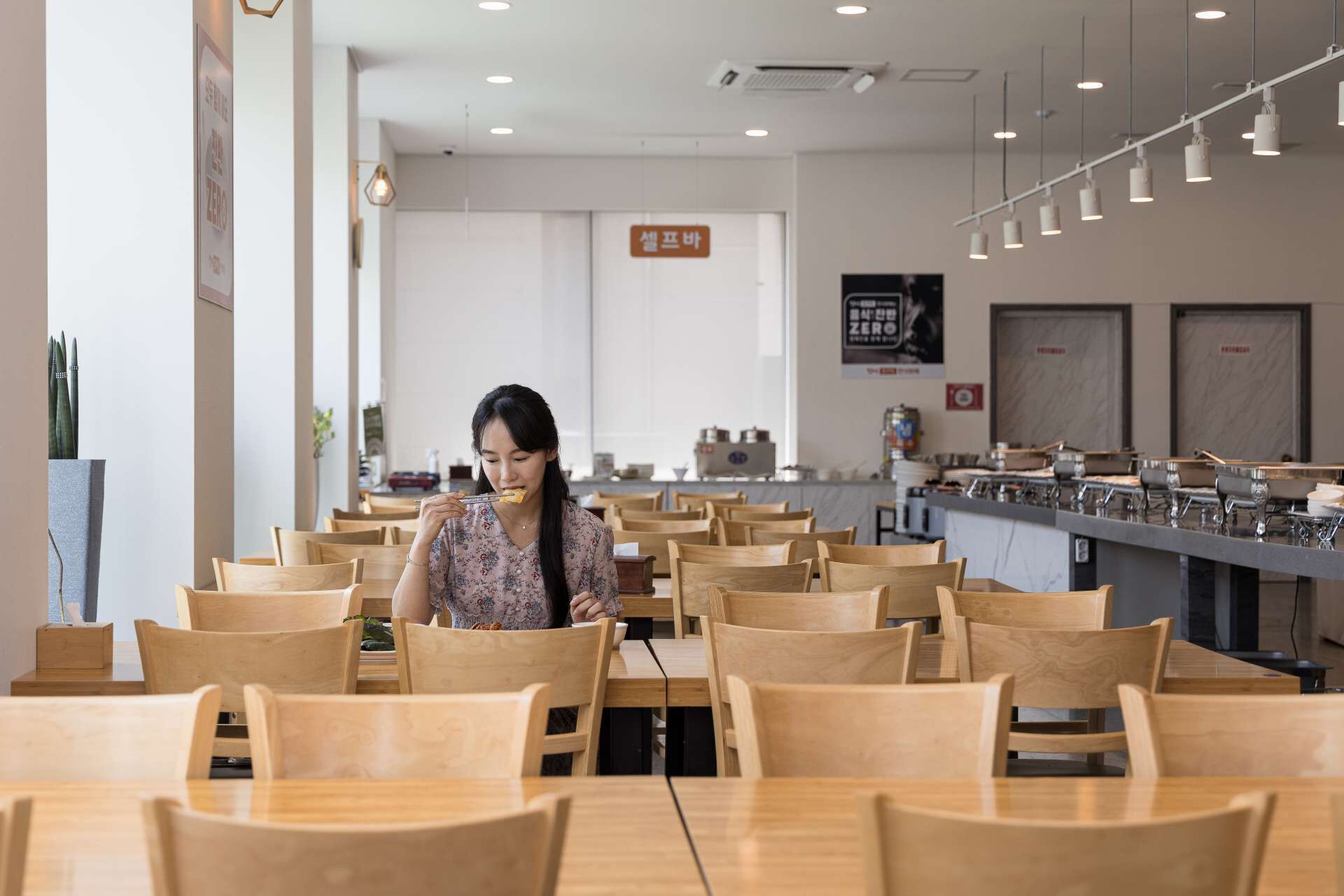 Un espace repas moderne avec des tables et des chaises en bois, un comptoir équipé pour la préparation et le service des aliments, et un panneau indiquant la possibilité de commander des plats végétariens.