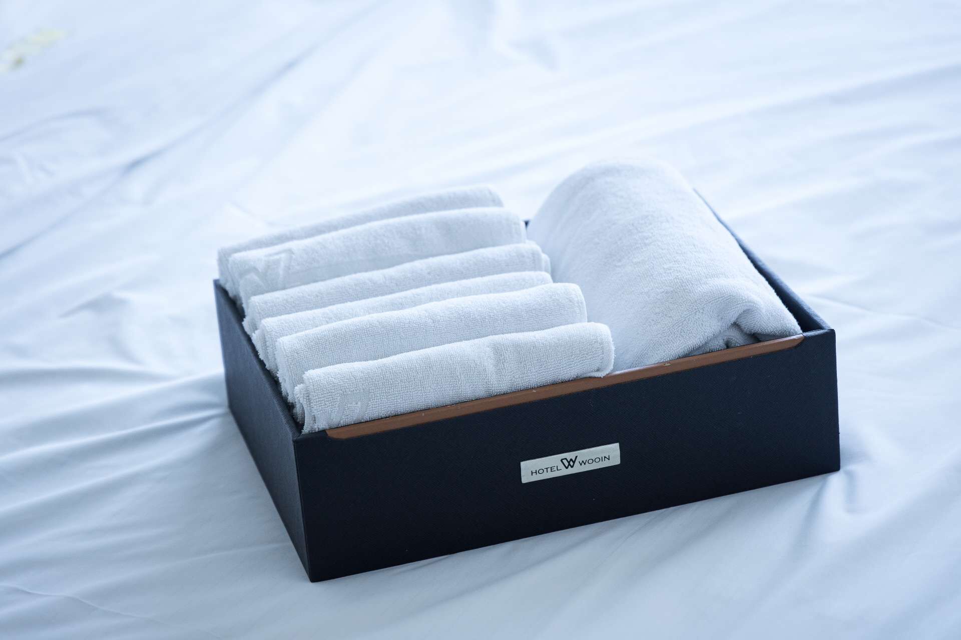 Eine schwarze Box mit Holzbasis, gefüllt mit sauber gefalteten weißen Handtüchern, beschriftet mit „HOTEL WOIN“.