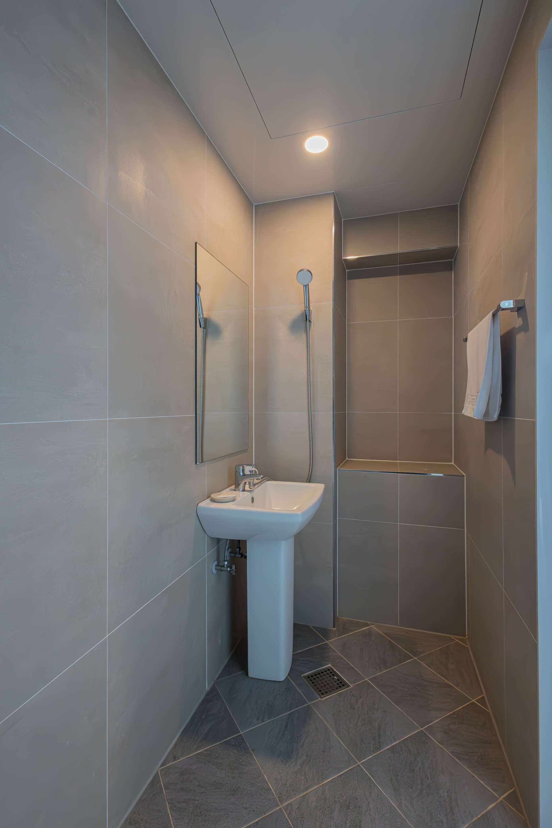 A modern bathroom with a white sink, a mirror, and a shower area.