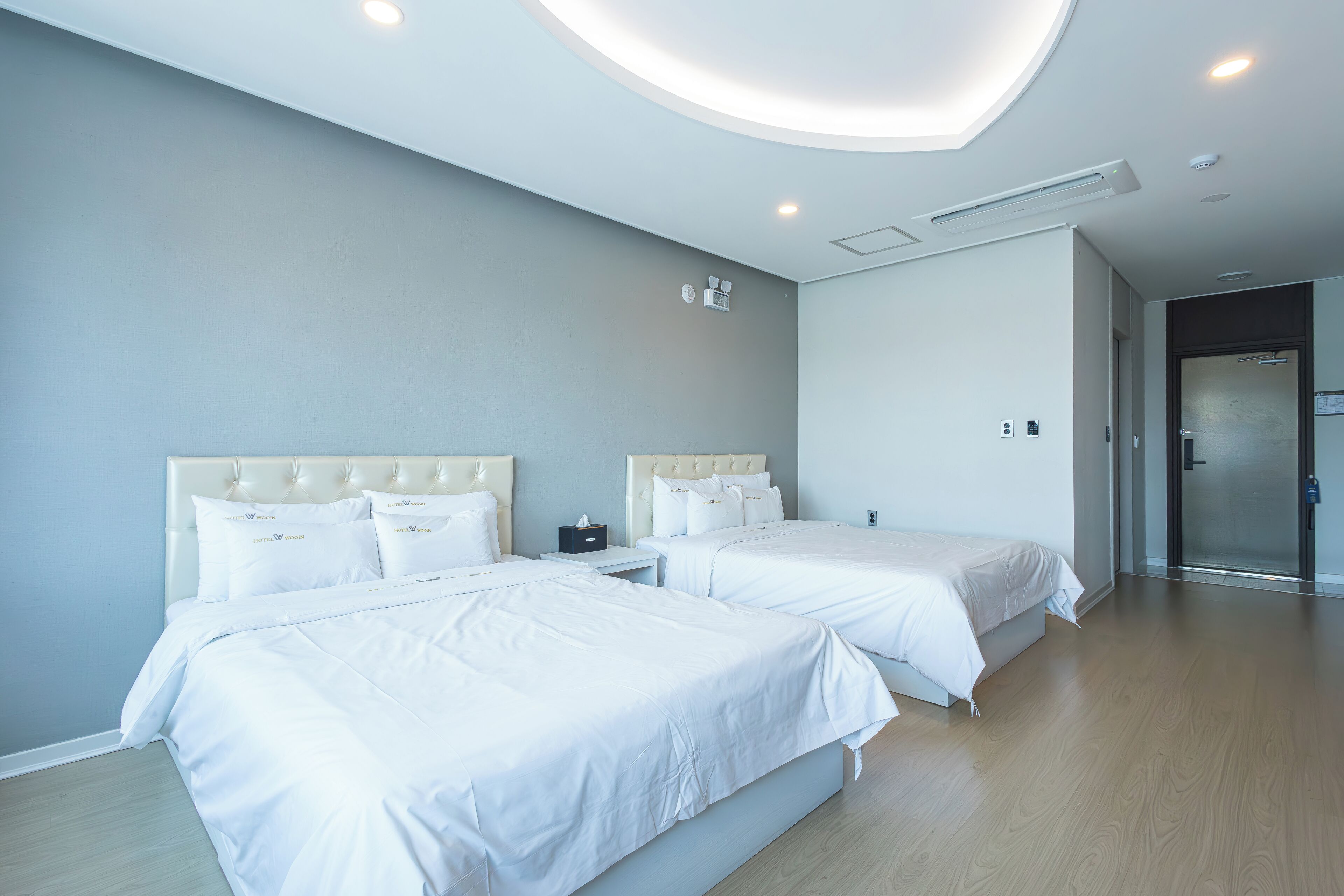 A modern hotel room with two beds, a round ceiling light, and a wooden floor.