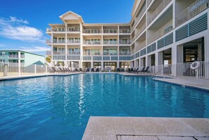Ein Hotel mit Schwimmbad, mehreren Balkonen und wolkenlosem, blauem Himmel.