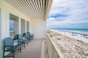 A balcony with Adirondack chairs, a wooden deck, and a view of a beach with umbrellas and people. - Stunning 1BR Sea Glass Unit 305 with Beautiful Gulf Front Views! (Gulf Shores)
