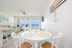 A bright living room with a dining area, large windows, and a ceiling fan. - Stunning 1BR Sea Glass Unit 305 with Beautiful Gulf Front Views! (Gulf Shores)