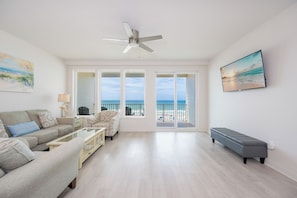 A spacious living room with a sofa, armchair, and bench, large windows with a view of the beach, and a ceiling fan. - Stunning 1BR Sea Glass Unit 305 with Beautiful Gulf Front Views! (Gulf Shores)