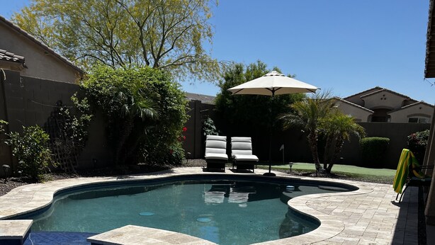 A swimming pool with a curved design, surrounded by stone tiles and gravel. There are lounge chairs and an umbrella in the background. - Great family friendly home very private back yard, heated pool & covered patio. (San Tan Valley)