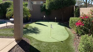 A backyard with a putting green, a pool, and a house with a covered patio. - Great family friendly home very private back yard, heated pool & covered patio. (San Tan Valley)