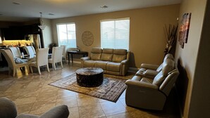 A spacious living room with a large sofa, a smaller sofa, and a recliner. There is a dining area with a table and chairs, and a kitchen in the background. - Great family friendly home very private back yard, heated pool & covered patio. (San Tan Valley)