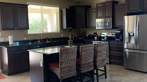A modern kitchen with dark cabinets, a stainless steel refrigerator, a microwave, and a large island with bar stools. - Great family friendly home very private back yard, heated pool & covered patio. (San Tan Valley)