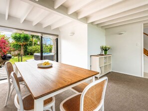 A modern dining area with a wooden table, white chairs, and a glass door leading to a garden. - Blackpool Bayside - Easy Walk to Oneroa (Oneroa)