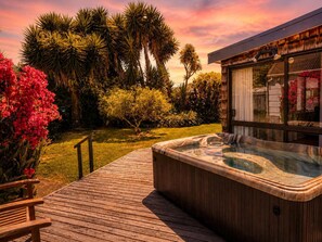 Eine Holzterrasse mit Whirlpool, umgeben von üppiger Vegetation und einem modernen Gebäude.