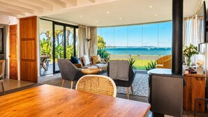 Ein modernes Wohnzimmer mit einem großen Holztisch, bequemen Sitzgelegenheiten, einem schwarzen Kamin und Blick aufs Meer.