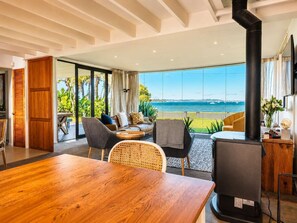 Un soggiorno moderno con un ampio tavolo in legno, sedute confortevoli, un camino nero e vista sul mare.