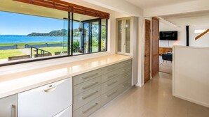 Eine moderne Küche mit einem großen Fenster und schöner Aussicht, eingebauten Schränken und einem an der Wand befestigten Flachbildfernseher.