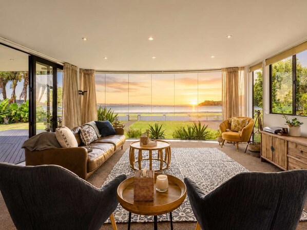 Ein großzügiges Wohnzimmer mit einem großen Fenster und Blick auf eine schöne Landschaft, einem bequemen Sofa, einem Couchtisch und zwei Sesseln.