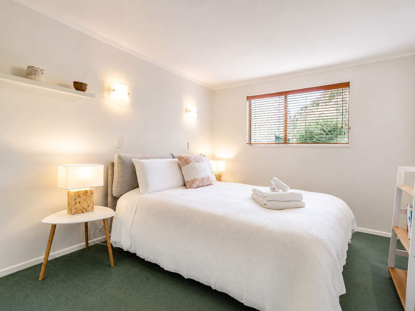 Une chambre à coucher avec un lit, une table de chevet, une lampe et une fenêtre avec des stores.