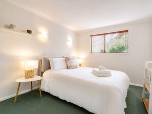 Ein Schlafzimmer mit Bett, Nachttisch, Lampe und einem Fenster mit Jalousien.