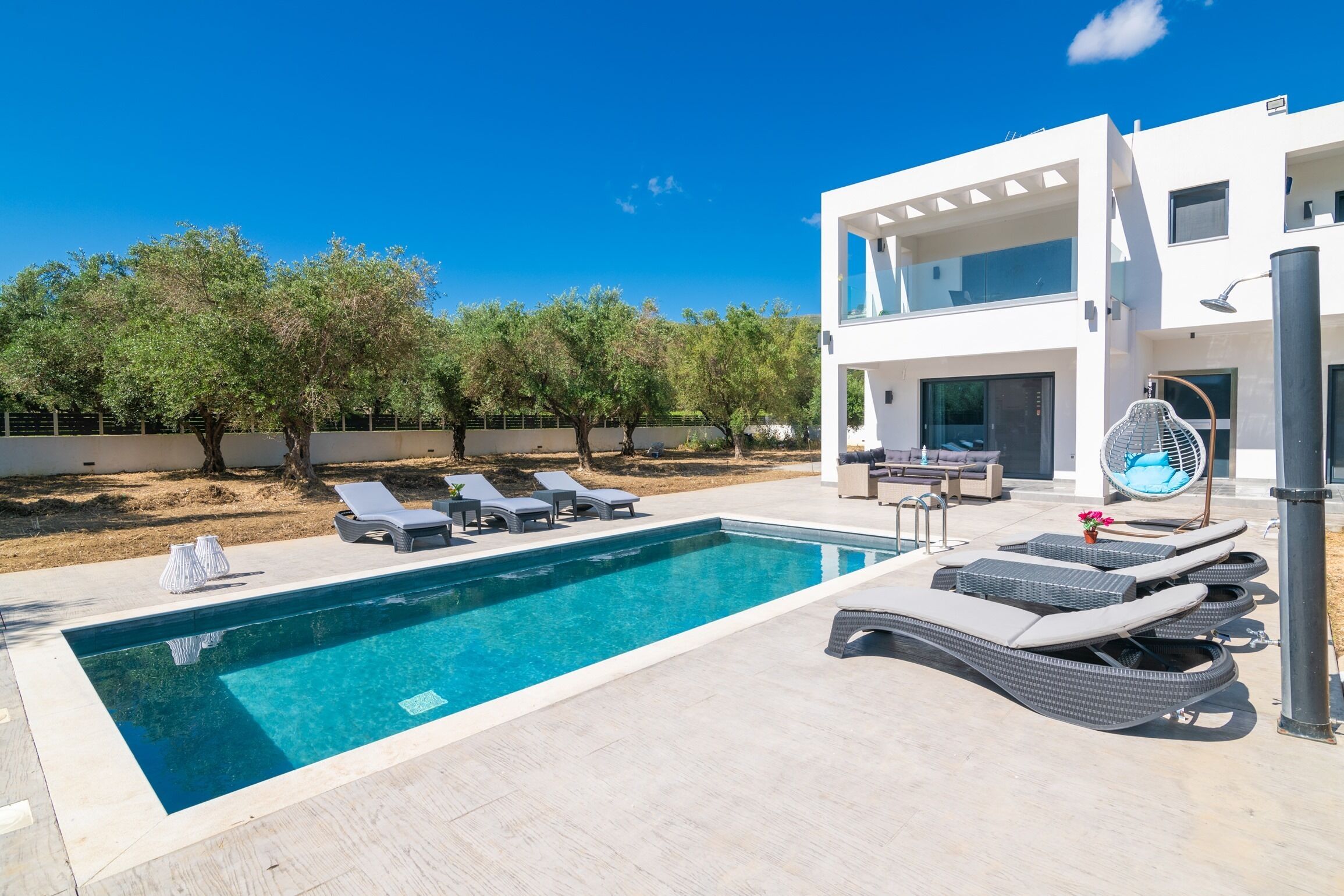 Una moderna casa a due piani con piscina, lettini prendisole e una zona relax coperta.