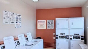 Een wasserette met meerdere wasmachines en drogers, informatieborden over de service en een eenvoudig droogsign.