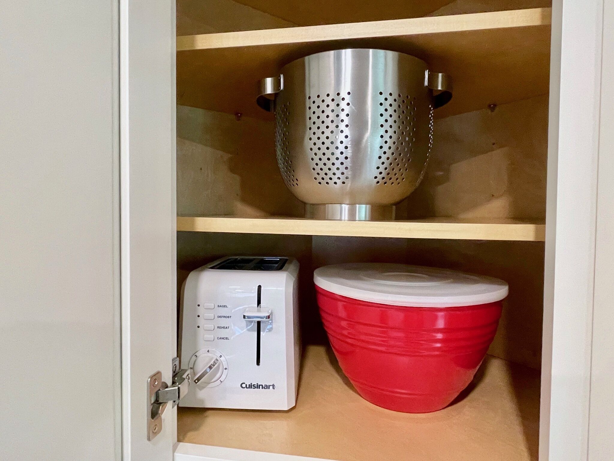 A kitchen cabinet with a toaster and a red bowl.