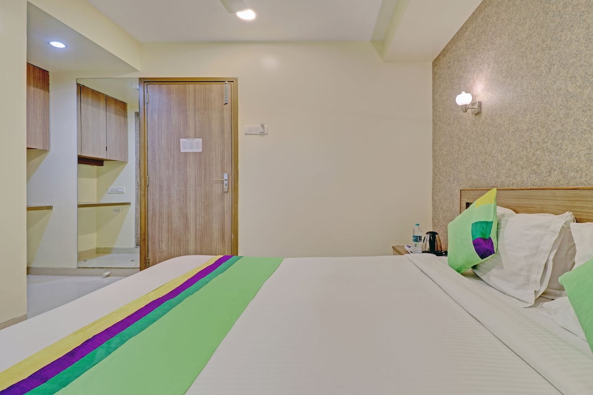 Habitación de hotel con cama, mesita de noche, botella de agua y lámpara fijada a la pared.
