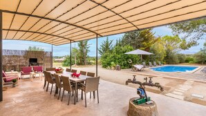 An outdoor patio with a table and chairs, a barbecue grill, a pool, and a water feature.