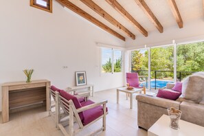 Un vaste espace de vie doté d’un plafond en bois, d’un canapé, d’un fauteuil, d’une petite table et offrant une vue sur une piscine.