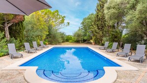 A rectangular swimming pool with a tiled edge, surrounded by lounge chairs and a pergola.