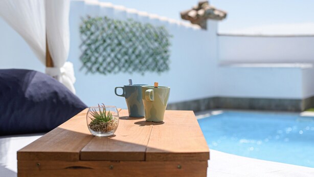 Ein Holztisch mit zwei Tassen und einer kleinen Pflanze mit Blick auf einen Swimmingpool.