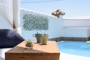 Une table en bois avec deux tasses et une petite plante, donnant sur une piscine.