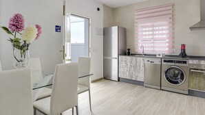 Eine moderne Küche mit Waschmaschine, Kühlschrank und Essbereich mit Stühlen und einem Glastisch.