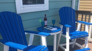 Une terrasse avec deux chaises Adirondack bleues et une petite table ronde, une bouteille de vin et deux verres.