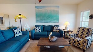 Un salon comprenant un canapé, un fauteuil, une table basse et un tableau représentant une vague.