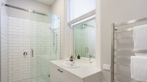A modern bathroom with a glass shower enclosure, a white sink with a mirror, and a towel rack.