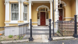 A yellow building with a red door, white columns, and a black iron fence.