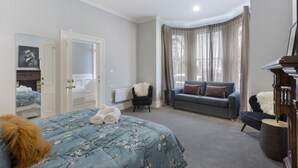 A bedroom with a bed, a sofa, a chair, a mirror, and a radiator.