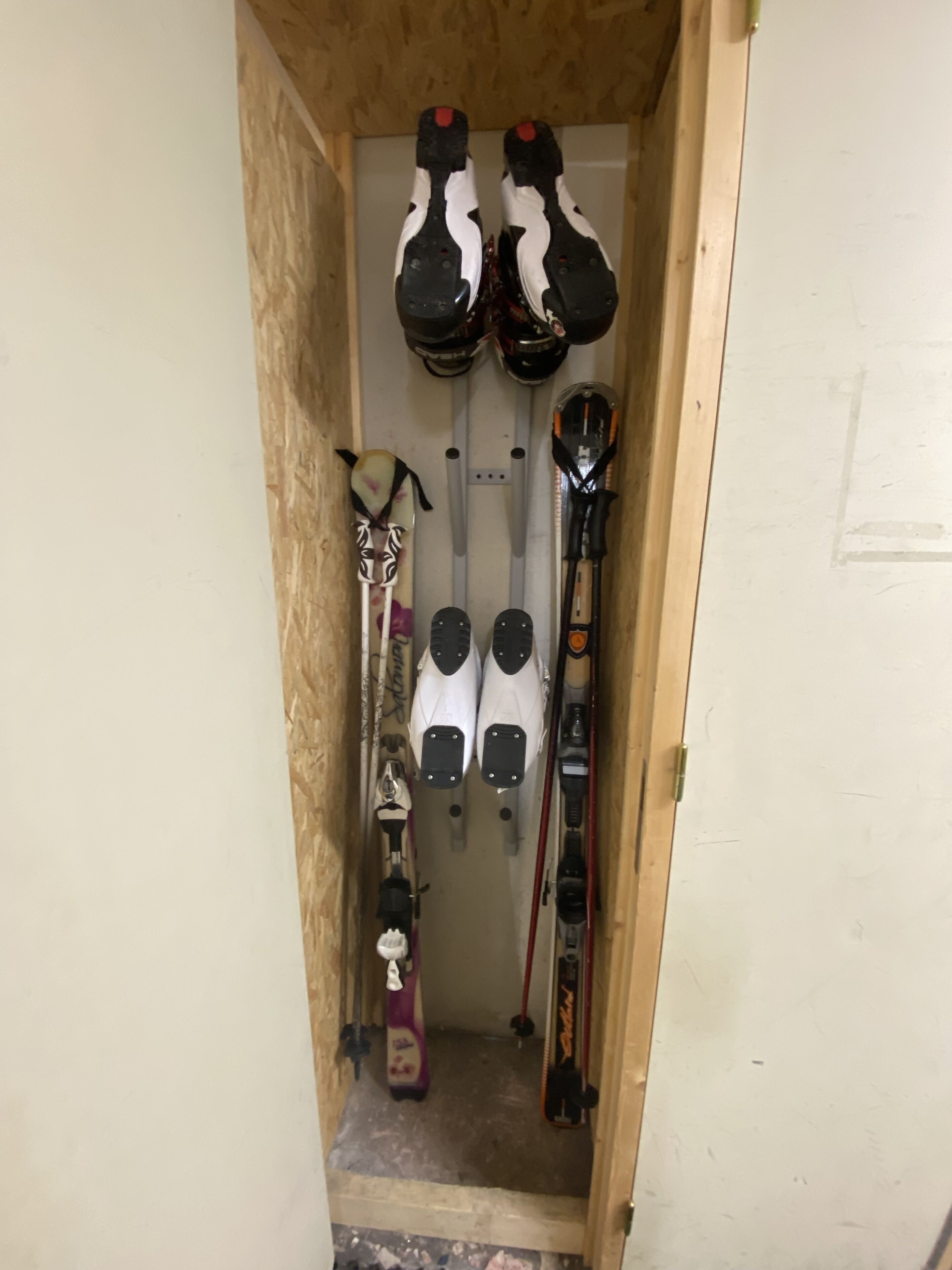 A narrow wooden storage area with skis and ski poles.