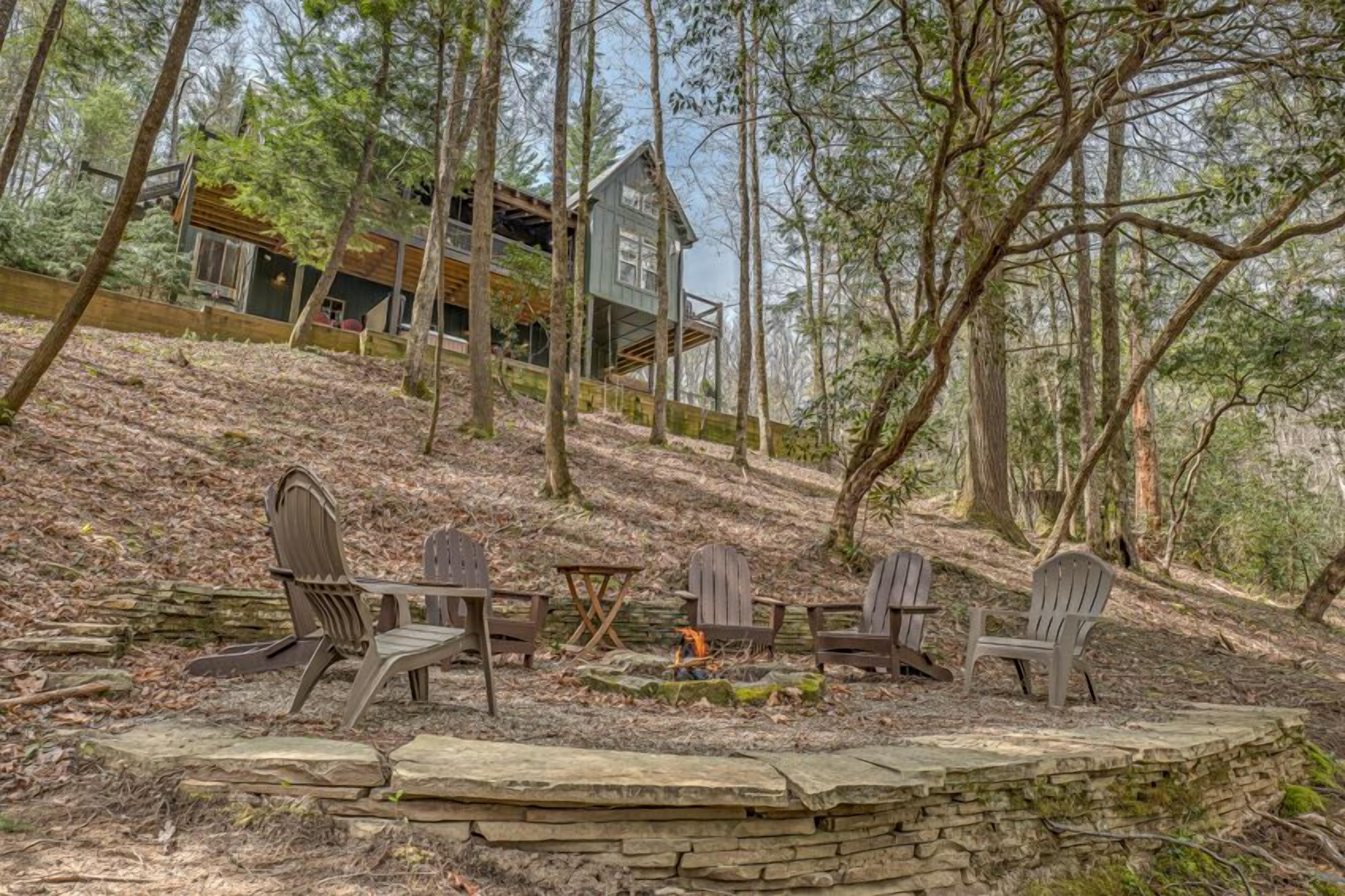 A cabin in a forest with outdoor seating and a fire pit.
