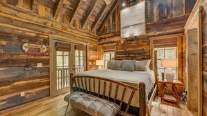Ein Schlafzimmer in einer Blockhütte mit einem hölzernen Bett, einer Bank und einem großen Fenster.