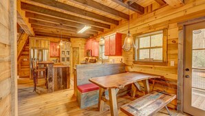 Ein rustikales Holzblockhaus-Interieur mit Küchenbereich, Esstisch aus Holz und einer Treppe, die zu einer oberen Ebene führt.