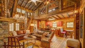 Ein rustikales Blockhaus-Interieur mit Kamin aus Stein, Holzmöbeln, einer Küchenzeile und einem Erkerraum.